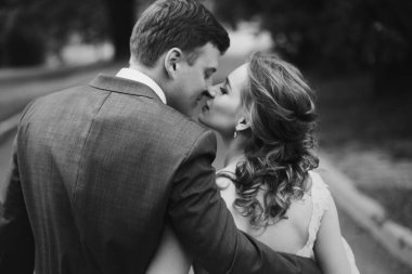 Sarılma ve açık havada yaz parkta öpüşme romantik yeni evli çift, düğün şık gelin elbise yürüyüşe ile yakışıklı damat