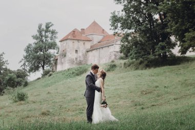 güzel güzel gelin ve damat öpüşme ve güneşli parkta yürüyüş. mutlu evlilik çift eski kale, yeşil bahçesinde sarılma. mutlu romantik anlar. kaçış kavramı