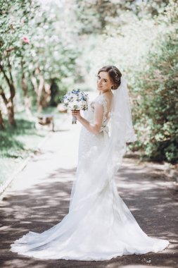 poz ve gülümseyen güneşli bahar parkta kokulu güzel muhteşem gelin. yeşil bahçesinde duran mutlu kadın. mutlu bir evlilik anlar. kaçış kavramı