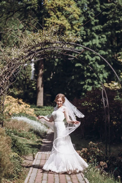 Romantik bahçe çiçek kemer ile beyaz gelinliği içinde dönen mutlu yeni evli gelin