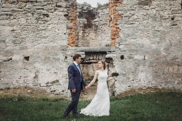古い城の壁の近くにポーズ新婚夫婦 古代の城の屋外でのおとぎ話の結婚式 要塞の塔の近くに抱擁新郎新婦 結婚式の瞬間 — ストック写真