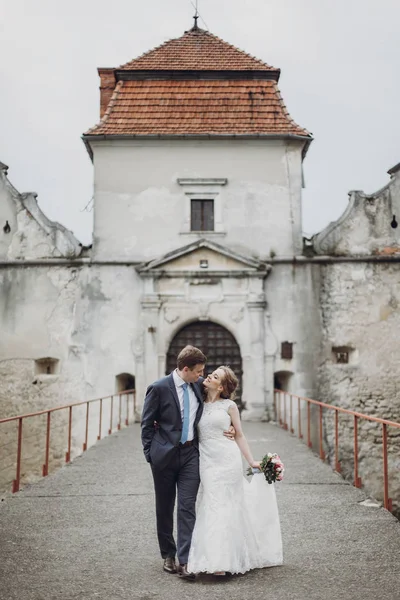 おとぎ話の結婚式の瞬間近くに歩いて新婚夫婦の幸せなカップル美しい花嫁と新郎はヨーロッパで古代の城入口近く抱っこ — ストック写真