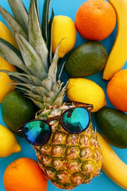 ananas şık güneş gözlüğü ve muz, portakal, avokado ve parlak mavi kağıt üzerine limon, trendy düz yatıyordu. metin için yer. renkli meyve modern resim, üstten görünüm. sulu yaz desen
