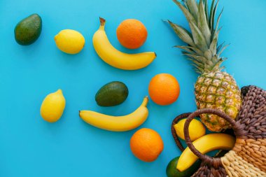 ananas, muz, portakal, limon ve avokado şık Eko Çanta trendy düz lay parlak mavi kağıda dağınık. metin için yer. renkli meyve modern resim, üstten görünüm. sağlıklı alışveriş