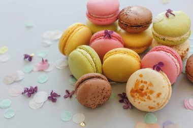 renkli macarons Lila çiçek ve konfeti ile trendy pastel gri kağıt üzerinde. pembe, sarı, yeşil ve kahverengi lezzetli Bademli kurabiye. parti için çikolata. Gıda Fotoğrafçılık. nefis arka plan