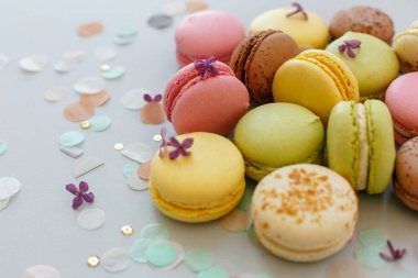 renkli macarons Lila çiçek ve konfeti ile trendy pastel gri kağıt üzerinde. pembe, sarı, yeşil ve kahverengi lezzetli Bademli kurabiye. parti için çikolata. Gıda Fotoğrafçılık. nefis arka plan