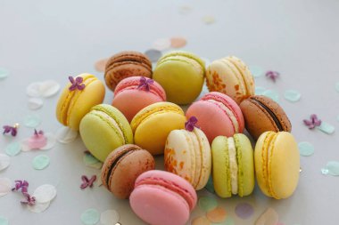renkli macarons Lila çiçek ve konfeti ile trendy pastel gri kağıt üzerinde. pembe, sarı, yeşil ve kahverengi lezzetli Bademli kurabiye. parti için çikolata. Gıda Fotoğrafçılık. nefis arka plan