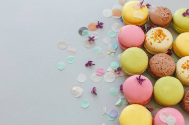 düz renkli macarons Lila çiçek ve konfeti ile trendy pastel gri kağıt üzerinde yatıyordu. pembe, sarı, yeşil ve kahverengi lezzetli Bademli kurabiye. parti için çikolata. gıda fotoğrafçılığı
