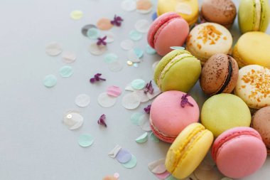 renkli macarons Lila çiçek ve konfeti ile trendy pastel gri kağıt üzerinde. pembe, sarı, yeşil ve kahverengi lezzetli Bademli kurabiye. parti için çikolata. Gıda Fotoğrafçılık. nefis arka plan