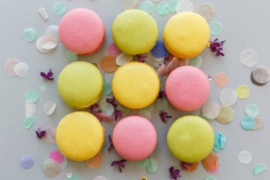 düz renkli macarons Lila çiçek ve konfeti ile trendy pastel gri kağıt üzerinde yatıyordu. pembe, sarı, yeşil ve kahverengi lezzetli Bademli kurabiye. parti için çikolata. gıda fotoğrafçılığı