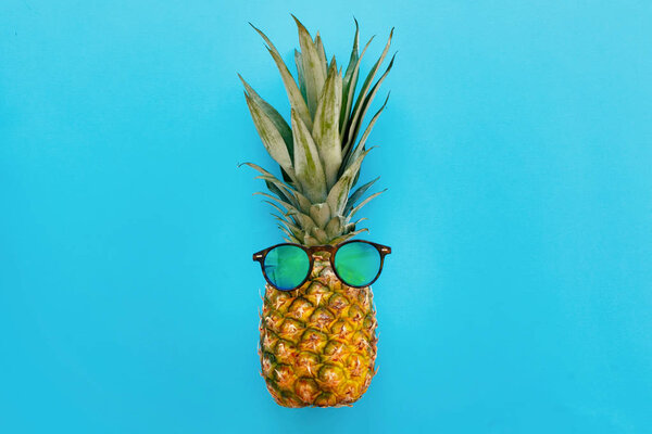 stylish hipster pineapple in sunglasses on trendy blue paper background. summer flat lay. vacation and party concept. space for text. summer relax, travel and holidays