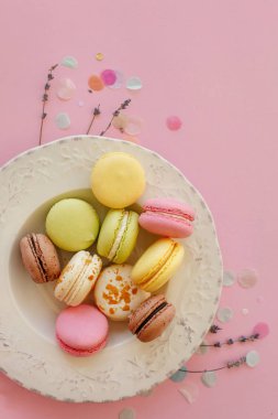 gıda fotoğrafçılığı düz lezzetli renkli macarons vintage moda pastel pembe kağıt tabakta lavanta ve konfeti ile yatıyordu. alanı metin pembe, sarı, yeşil, beyaz, kahverengi macaroons için.