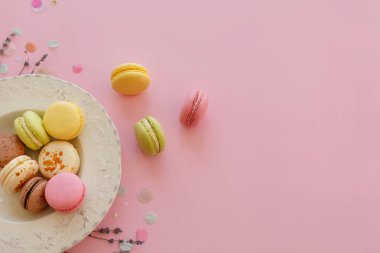 gıda fotoğrafçılığı düz lezzetli renkli macarons vintage moda pastel pembe kağıt tabakta lavanta ve konfeti ile yatıyordu. alanı metin pembe, sarı, yeşil, beyaz, kahverengi macaroons için.
