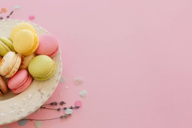 lezzetli renkli macarons lavanta ve konfeti ile trendy pastel pembe kağıt üzerinde vintage plaka. metin pembe, sarı, yeşil, beyaz, kahverengi macaroons için alan. modern gıda fotoğrafçılığı