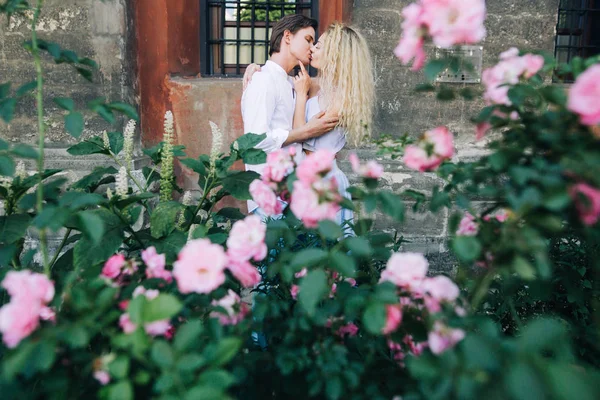 日当たりの良い咲く通りに優しく抱いて愛の美しいカップル スタイリッシュな流行に敏感な新郎と金髪の花嫁を採用します 夏にバカンスの街のロマンチックな瞬間 — ストック写真