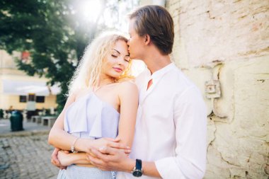 yürüyüş ve yavaşça güneşli yeşil sokak sarılma aşık güzel mutlu çift. kucaklayan şık hipster damat ve sarışın gelin. yaz şehir tatile sokak romantik anlar