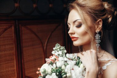 modern buket penceresinden ışık sabah otelin poz ile şık sarışın gelin. Düğün günü kavramı. güzel kadın portre beyaz elbiseli şaşırtıcı küpeli