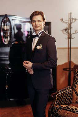 Aynaya bakmak şık damat papyon ve mavi takım otelin, sabah hazırlanıyor. Düğün günü kavramı. yakışıklı adam hazırlıklar vintage odasında smokin yaka çiçeği ile