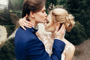 şık gelin ve damat kucaklayan ve parkta öpüşme. tutkulu lüks düğün çifti sarılma. Romantik duygusal an. adam mavi takım elbise ve açık havada beyaz elbiseli kadın