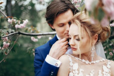 şık gelin ve damat kucaklayan ve manolya çiçekleri arasında parkta öpüşme. tutkulu lüks düğün çifti sarılma. Romantik duygusal an.