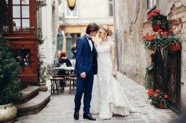 şık gelin ve damat yürüyüş ve şehir sokak kucaklayan. Lüks düğün çifti sarılma. Romantik duygusal an. Lviv beyaz elbiseli kadınla öpüşürken mavi elbiseli adam