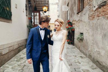 şık gelin ve damat yürüyüş ve şehir sokak kucaklayan. Lüks düğün çifti sarılma. Romantik duygusal an. Beyaz elbiseli kadınla öpüşürken mavi elbiseli adam