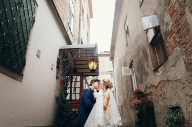 şık gelin ve damat yürüyüş ve şehir sokak kucaklayan. Lüks düğün çifti sarılma. Romantik duygusal an. Lviv beyaz elbiseli kadınla öpüşürken mavi elbiseli adam