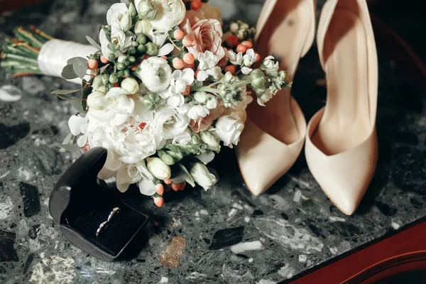 wedding concept. stylish shoes, golden wedding rings in a box and modern bouquet on marble background. luxury rings with diamond and fresh flowers on wedding morning. space for text