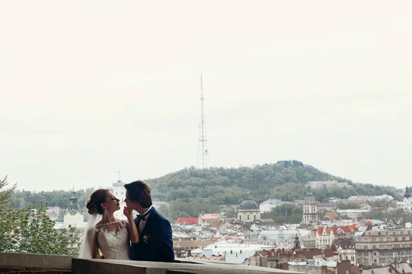 スタイリッシュな花嫁と花婿市ヨーロッパのリヴィウの背景にポーズします 幸せな贅沢な結婚式のカップルを受け入れ お互いを見ています ロマンチックな官能的な瞬間 — ストック写真