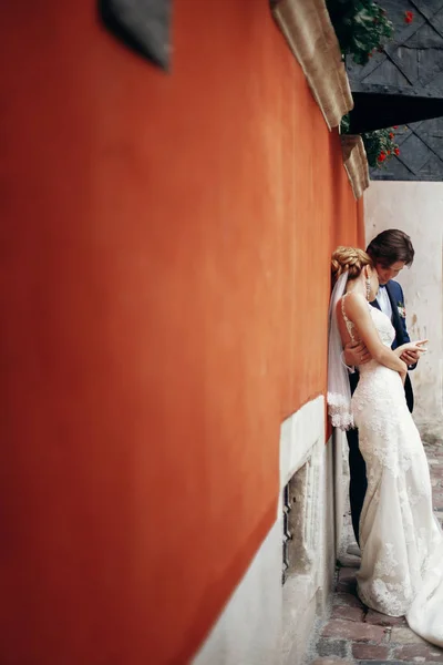豪華な結婚式のカップル古い建物の壁で抱き締めます スタイリッシュな花嫁と花婿を受け入れ 都市通りでキスします ロマンチックな官能的な瞬間 白いドレスの女性をキスをする男性 — ストック写真