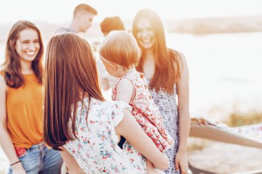Eller, annesi ve sahilde, herkes gülümseyerek arkadaşları ile bir yürüyüş kızı, sevimli küçük kız ile güzel genç anne