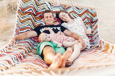 Mutlu aile portresi, Genç hipster baba ve anne bebek kızları, yaz tatili aile gezisi kavramı ile bir hamakta yalan