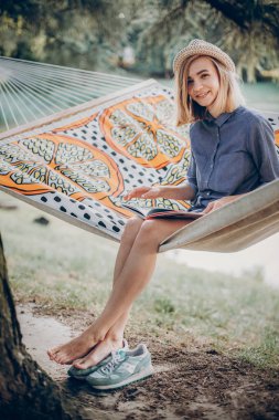 kitap okuma ve hamak güneşli yaz Park'ta rahatlatıcı şık hipster kadın. Tam boy
