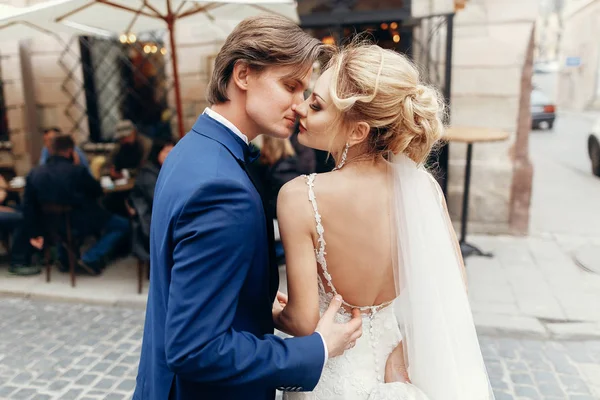 luxury wedding couple embracing at old building in light. stylish bride and groom kissing and hugging in city street. romantic sensual moment. man tenderly touching woman