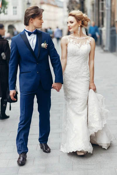 スタイリッシュな花嫁と花婿の街の通りを歩いてします 幸せな贅沢な結婚式を保持している光の手 ロマンチックな官能的な瞬間 男と女のお互いを見て — ストック写真