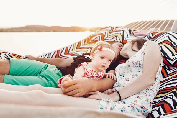 可爱的小女孩震惊的脸 躺在她的幸福的父亲和母亲 年轻的时髦夫妇放松与女儿在吊床上 可爱的吓坏了婴儿 — 图库照片