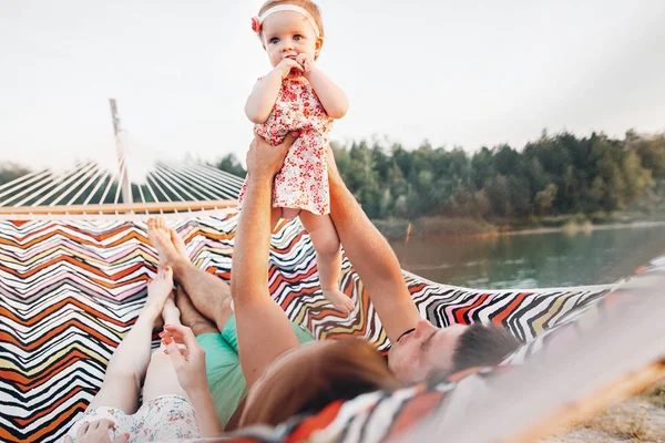 可爱的女孩在时髦的礼服与她的父母躺在湖和森林附近的吊床上的家庭度假旅行 可爱的时髦家庭与女儿 — 图库照片