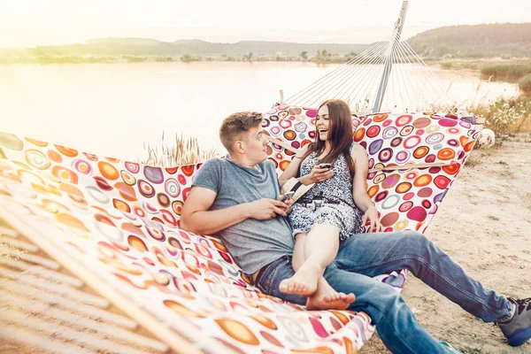 Happy Couple Looking Phones Smiling Relaxing Hammock Sunset Light Beach — Stock Photo, Image