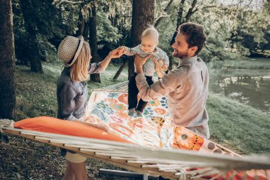 mutlu hipster aile yaz güneşli park hamakta şirin küçük oğlu ile oynamak. şık Anne ve baba ile çocuk ormanda rahatlatıcı ve gülüyor, eğleniyor. metin için yer. Aile Tatil