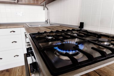 blue gas burning from stylish stove. close-up flames on modern cooker in  stylish light grey kitchen interior with modern furniture and stainless steel appliances in a new house clipart