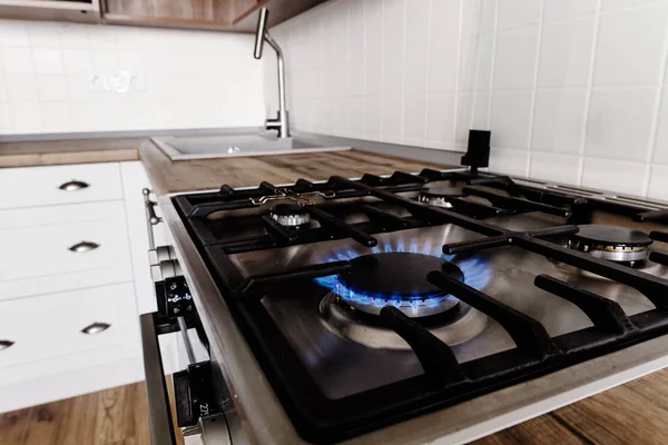 蓝色气体燃烧的时尚炉子 现代炊具的特写火焰在时髦的浅灰色厨房内部与现代家具和不锈钢用具在新的房子里 — 图库照片