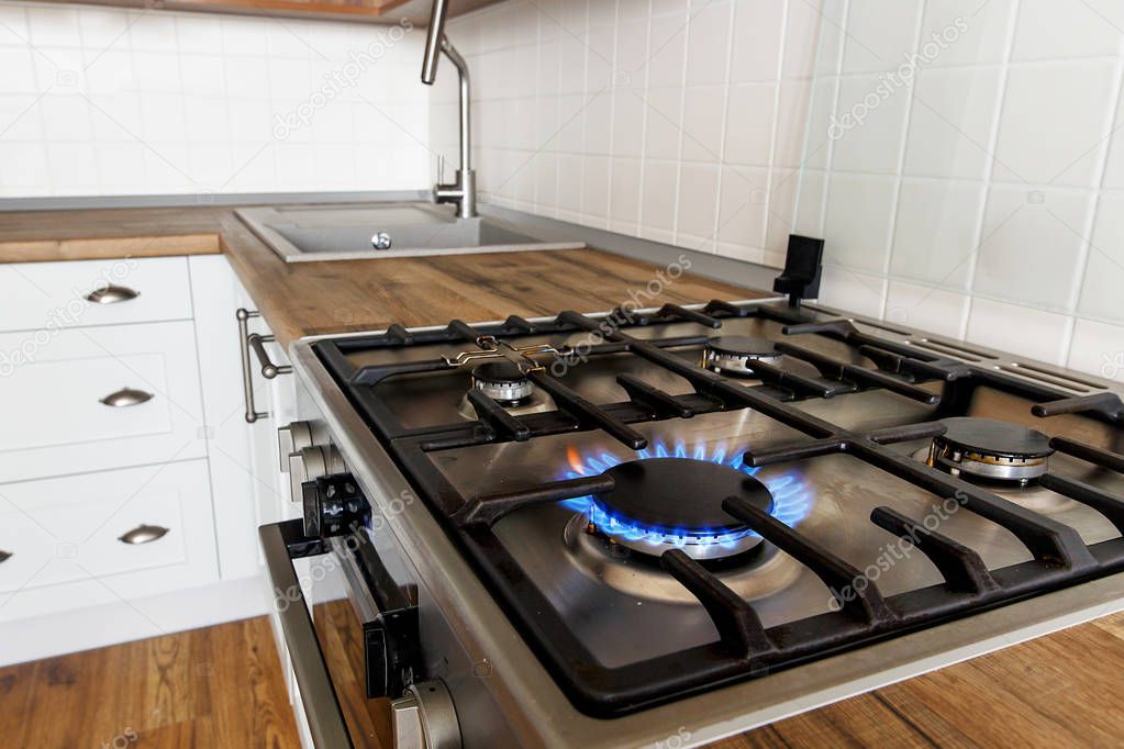 burning gas from kitchen stove on background of stylish kitchen interior with modern cabinets and stainless steel appliances. flames from modern cooker. design in scandinavian style