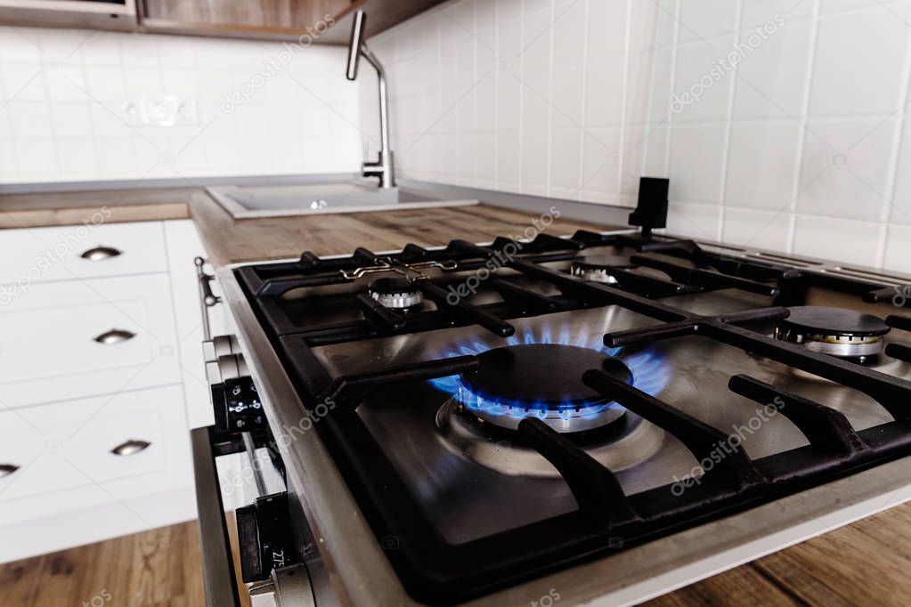 blue gas burning from stylish stove. close-up flames on modern cooker in  stylish light grey kitchen interior with modern furniture and stainless steel appliances in a new house