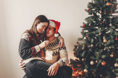 şık kaç sarılma ve gülümseyerek, rahat akşam fener ile Noel ağacı ışık tutan kazak içinde. atmosferik anlar, Noel Baba şapkalı adam. mutlu Noeller ve mutlu yeni yıl kavramı