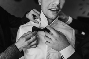 Damat odaya sabah sağdıç ile hazırlanıyor. adam üzerine koyarak ceket ve papyon, otel ışık penceresinde ayakta eller. Düğün günü için hazırlık