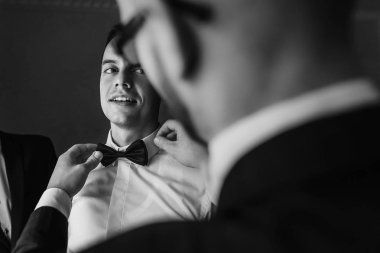 Damat odaya sabah hazırlanıyorum yardım sağdıç. adam üzerine koyarak ceket ve papyon, otel ışık penceresinde ayakta eller. Düğün günü için hazırlık