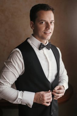 Damat odaya sabah hazırlanıyor. adam üzerine koyarak ceket ve papyon, otel ışık penceresinde ayakta eller. Düğün günü için hazırlık