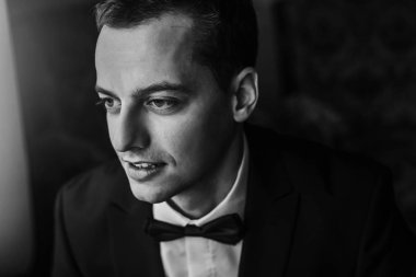 Sabahları yakışıklı damat portre odasında. mutlu adam gülümseyerek, otel ışık penceresinde ayakta papyon ile takım elbiseli. Düğün günü için hazırlık