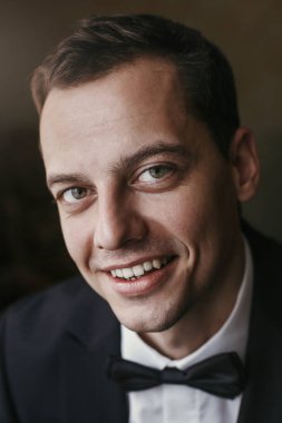 Sabahları yakışıklı damat portre odasında. mutlu adam gülümseyerek, otel ışık penceresinde ayakta papyon ile takım elbiseli. Düğün günü için hazırlık