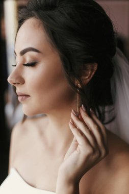 Lüks küpe üzerinde koyarak muhteşem gelin. güzel bir kadın portresi düğün için hazırlanıyor. duygusal bir an. seksi kız poz. Düğün takı aksesuar
